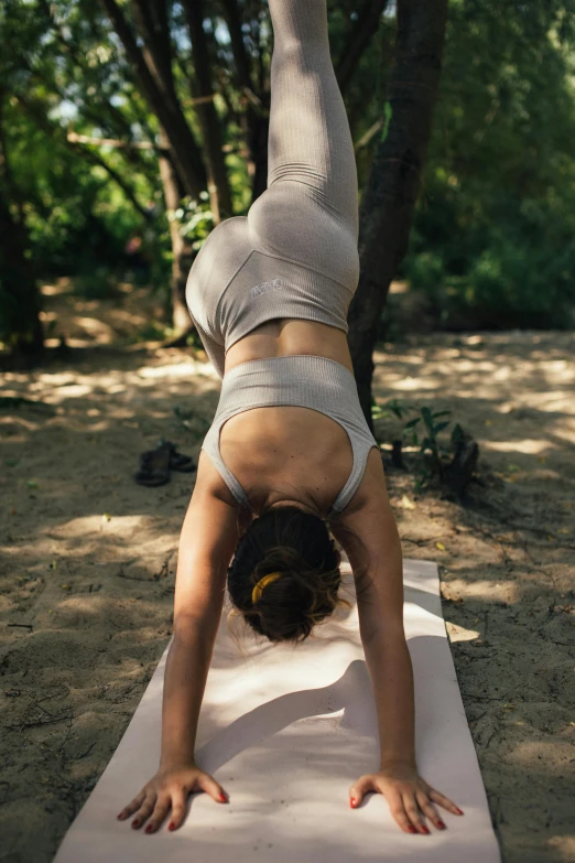 a woman is doing a handstand on a mat in the forest