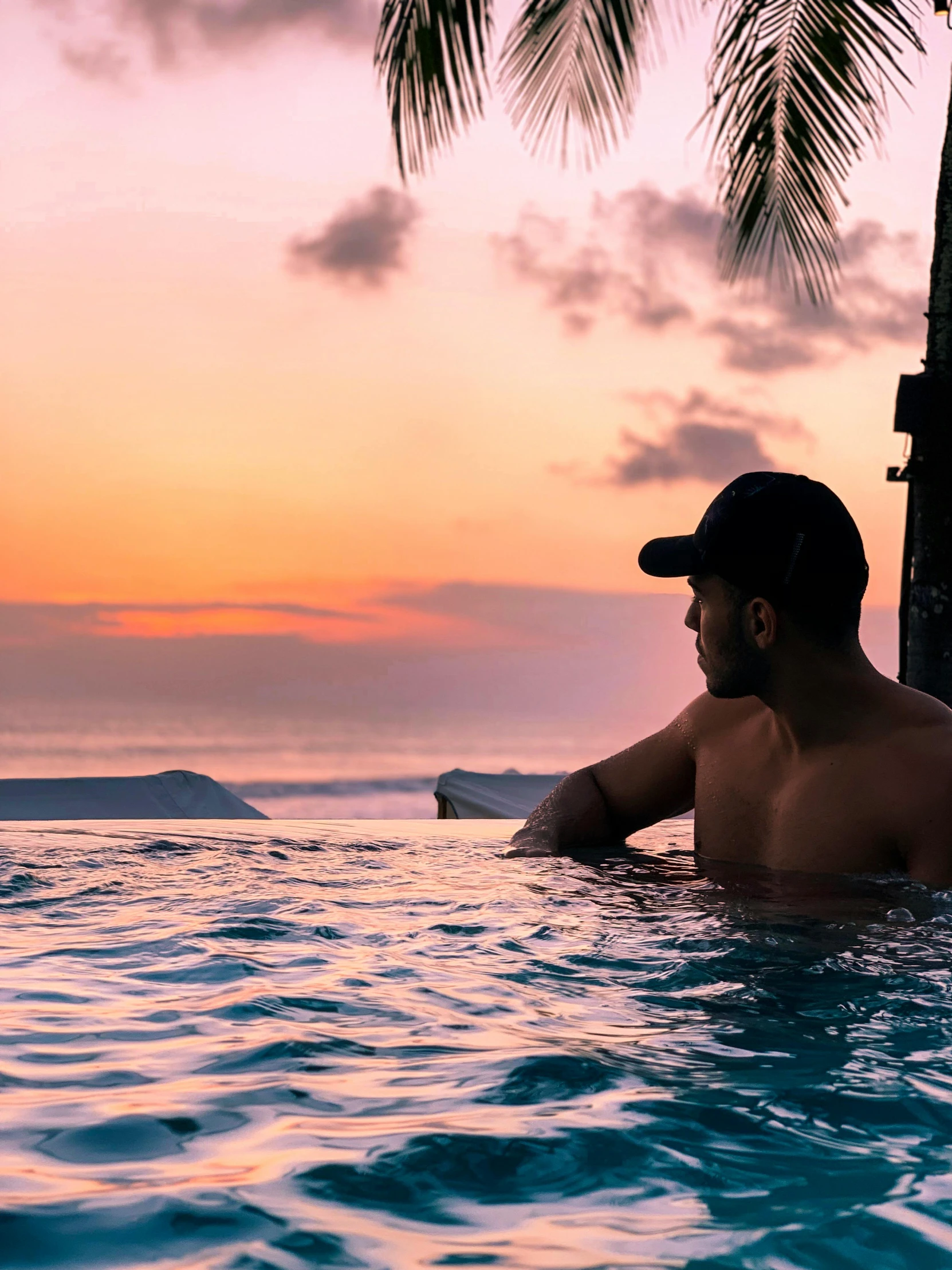 man in water pool with palm trees during sunset