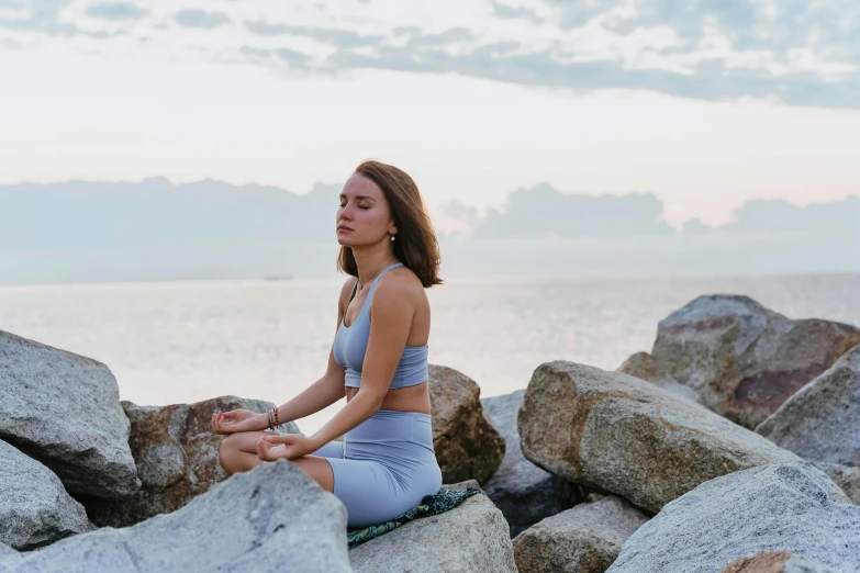 a beautiful young woman sitting on top of rocks next to the ocean