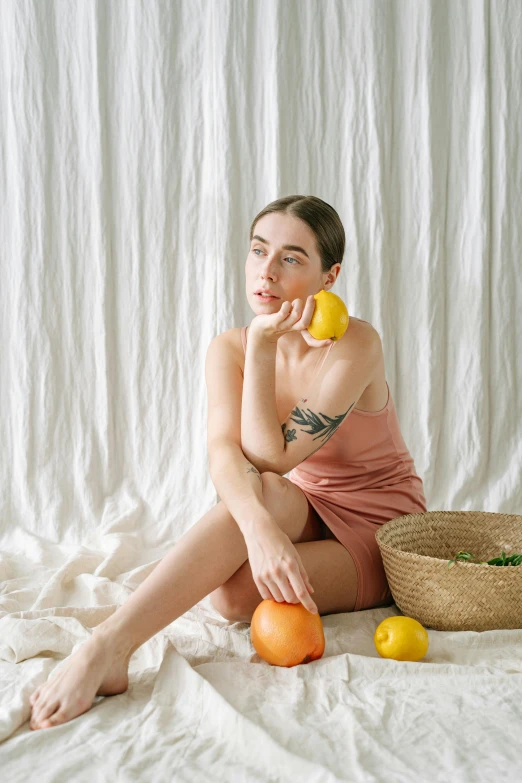 a young lady with tattoos sitting on a bed while holding an orange