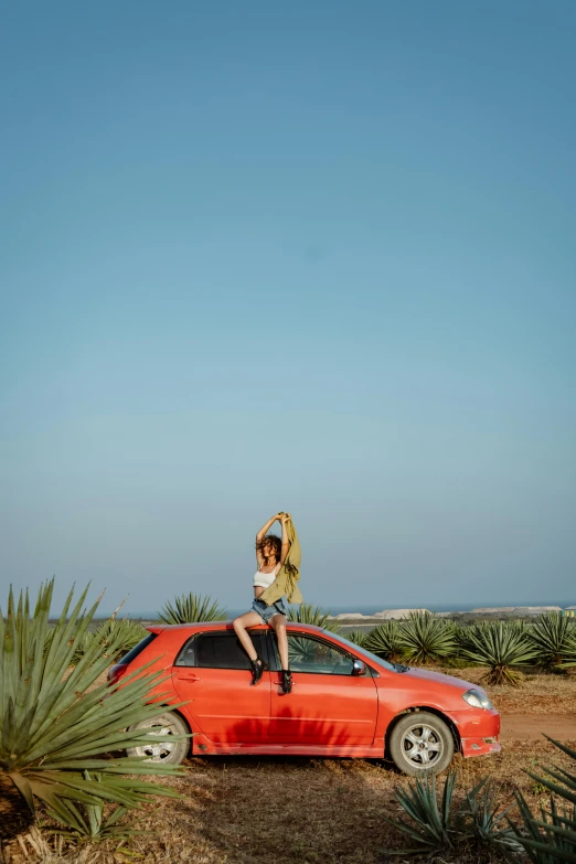 the car is sitting in a desert area, and the woman is standing on the top of it