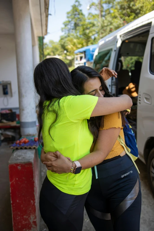 two women hugging each other next to a van