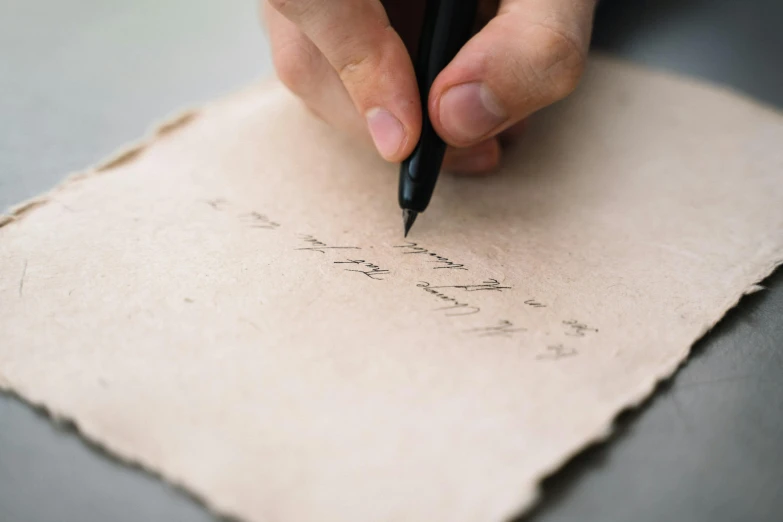 a person is writing with black pen on parchment paper
