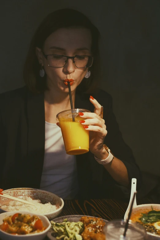 a woman drinking a beverage in front of a bowl full of food