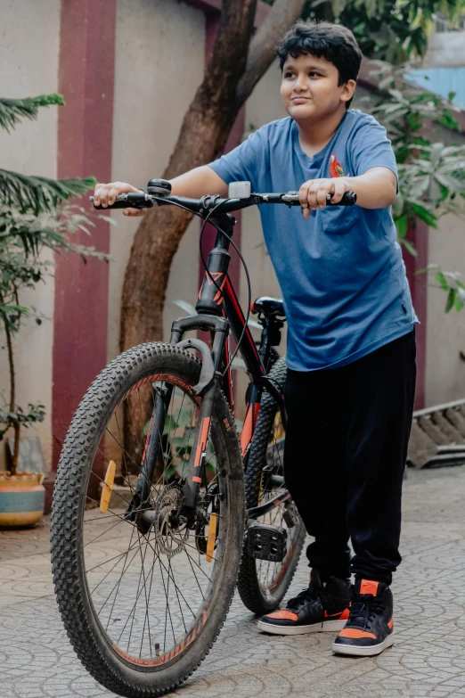 the boy stands with his bike outside, holding on