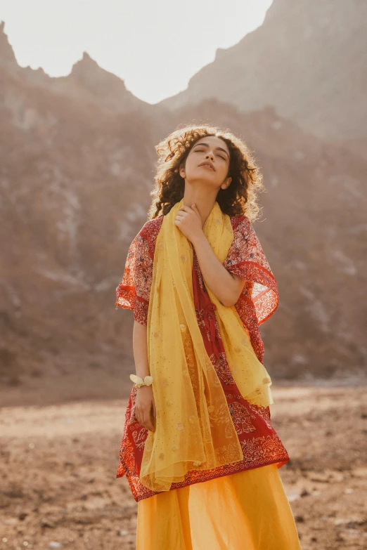 a young woman posing in a yellow outfit, with mountains in the background