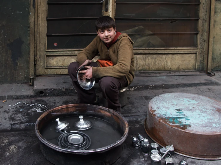 a young man sitting next to some metal pans