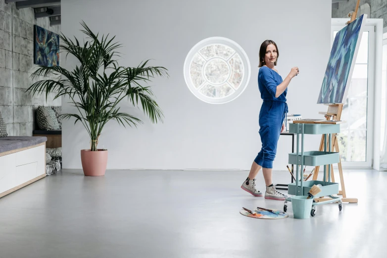 woman in blue doing art while standing in front of a painting