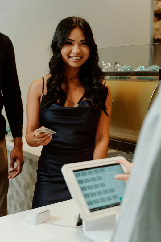 a woman in black dress smiling at a person holding an ipad