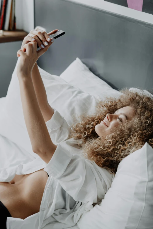 a lady laying on her back in bed while holding a phone