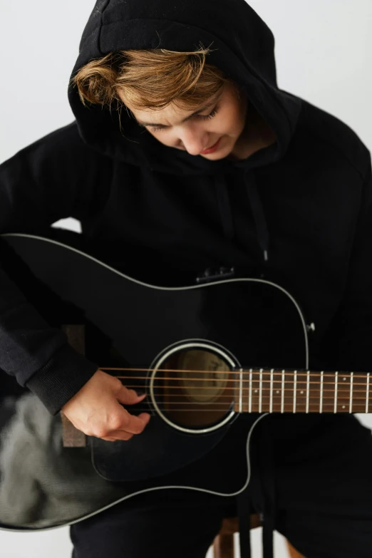 a boy is playing a guitar while wearing black