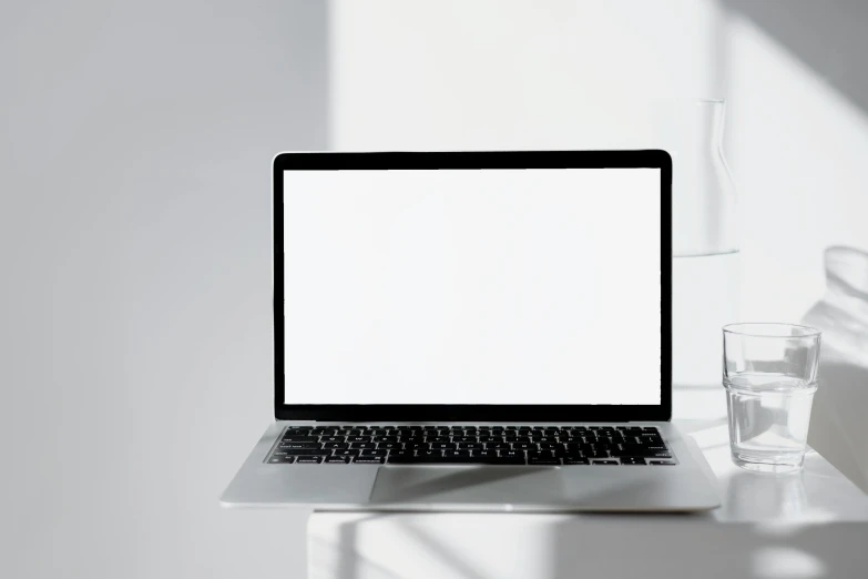 a lap top computer next to a glass of water on a white table