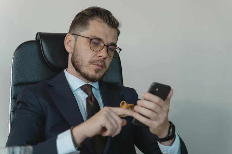 a man in a suit sitting in a chair holding a cell phone