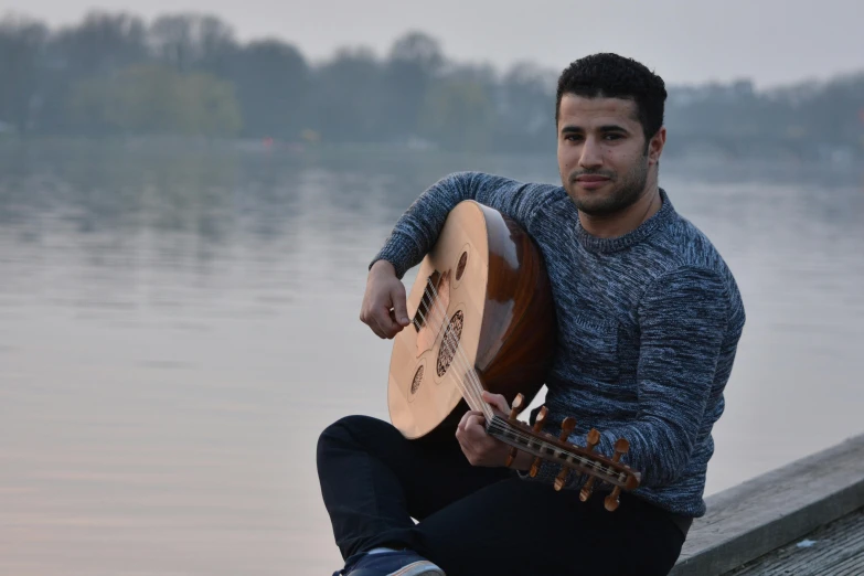 a man is holding a guitar by the water