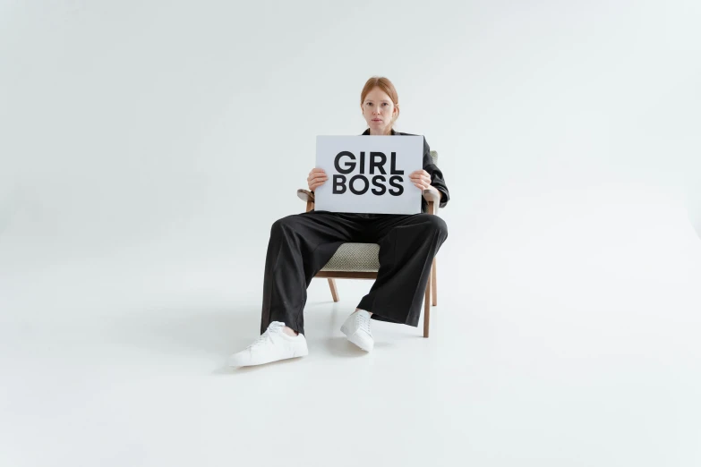 a young lady sitting on a chair holding a sign