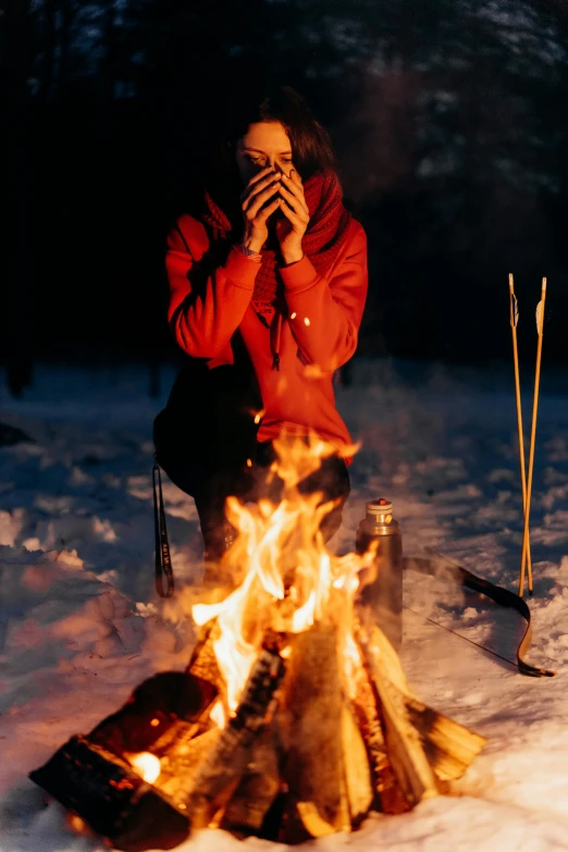 a woman sitting around a campfire while covering her face