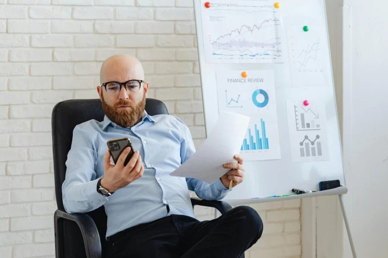 a man wearing glasses holds his cell phone near a whiteboard