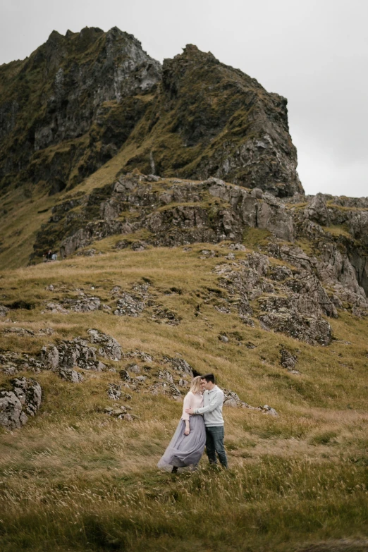 man and woman in white outfits emce on grassy area next to rocks