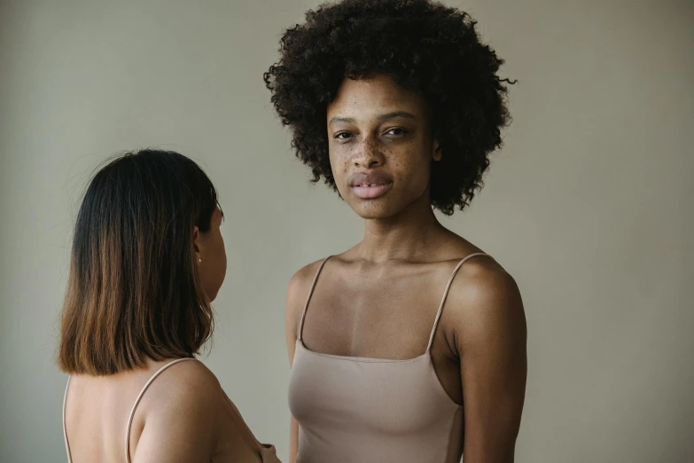 a woman standing by a mirror looking at another women