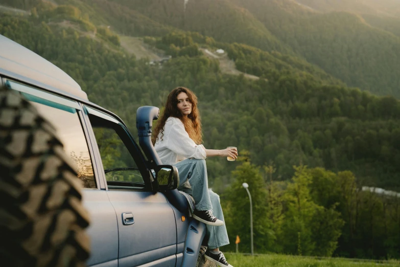 a woman sitting on the window of a car while standing next to a green truck