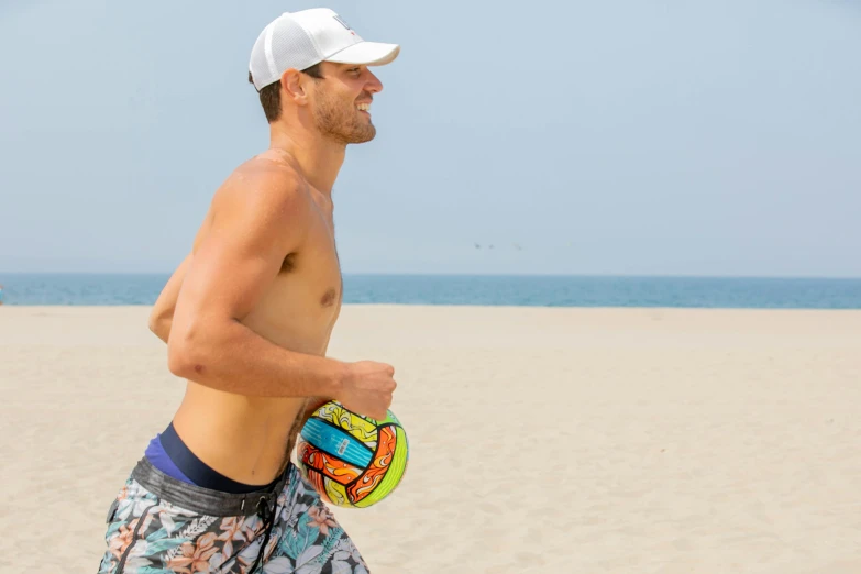 a shirtless man walking on the beach holding a frisbee