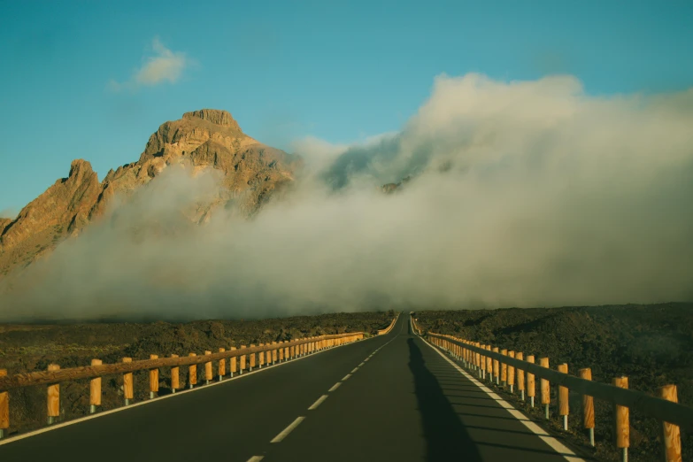 a road with a view of a mountain in the distance with low clouds on it