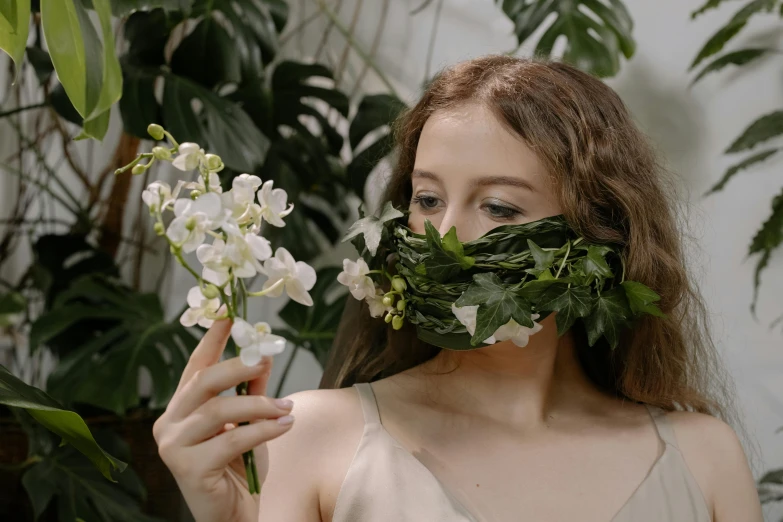 a beautiful young woman holding a plant as she looks through a piece of cut leaf