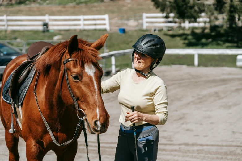 a woman wearing a helmet standing beside a horse