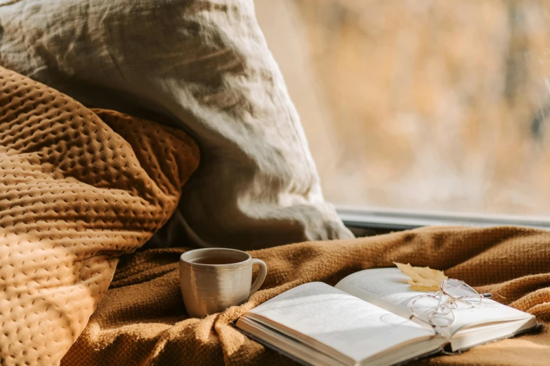 an open book with a coffee mug on the bed