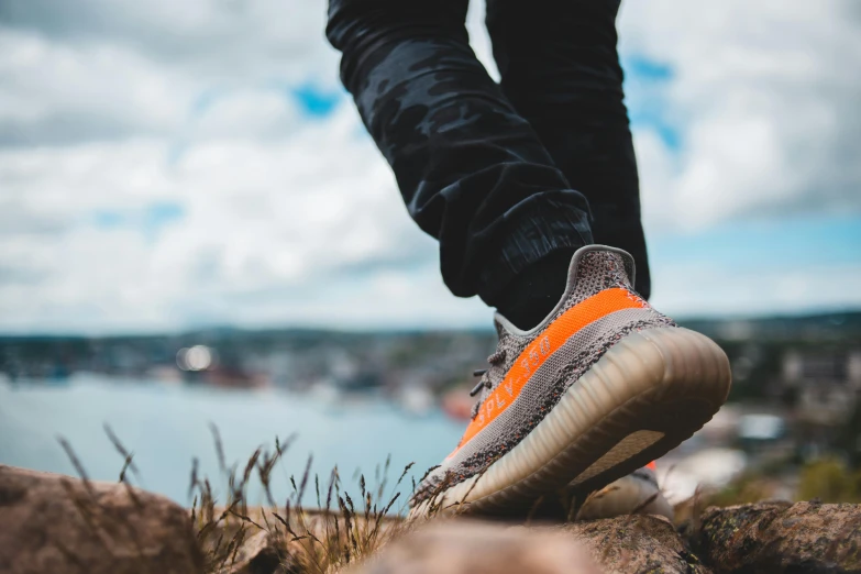 someone in sneakers standing on rocks by water