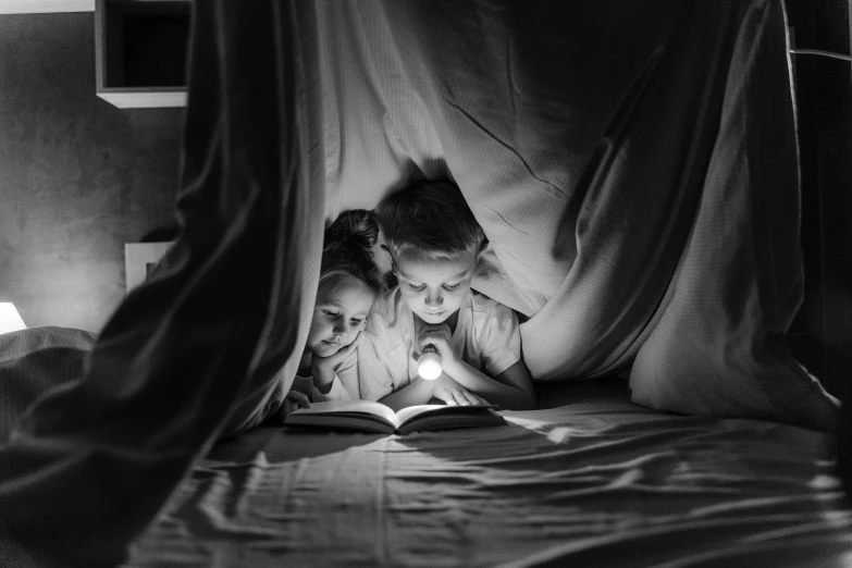 two girls in bed look down at the pages of a book