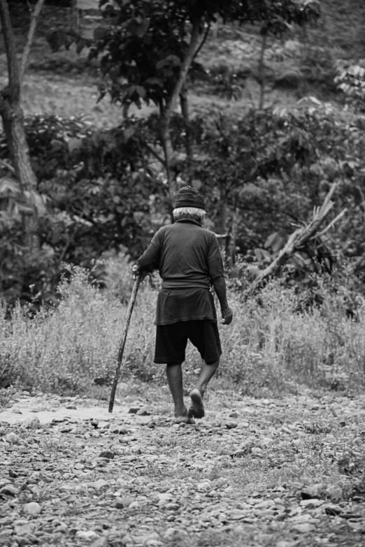a man walking in the grass with sticks in his hand
