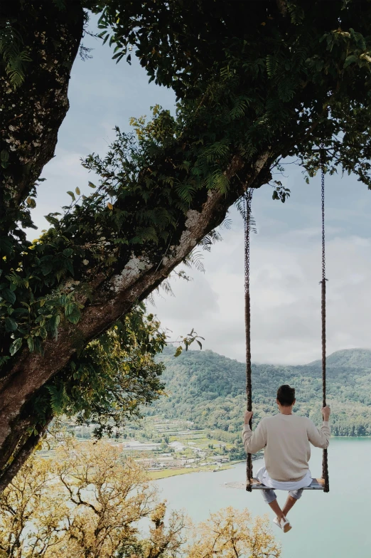 a man sits on a swing near a body of water