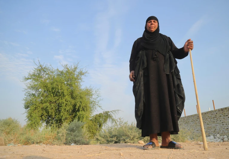 an afghan woman wearing traditional black is standing with her broom and poles