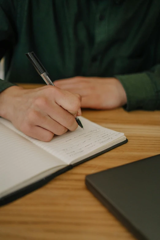 a person is writing on a paper in front of a laptop