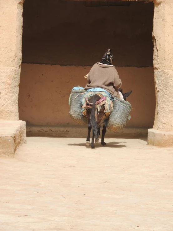 man riding a donkey in front of an adobe building