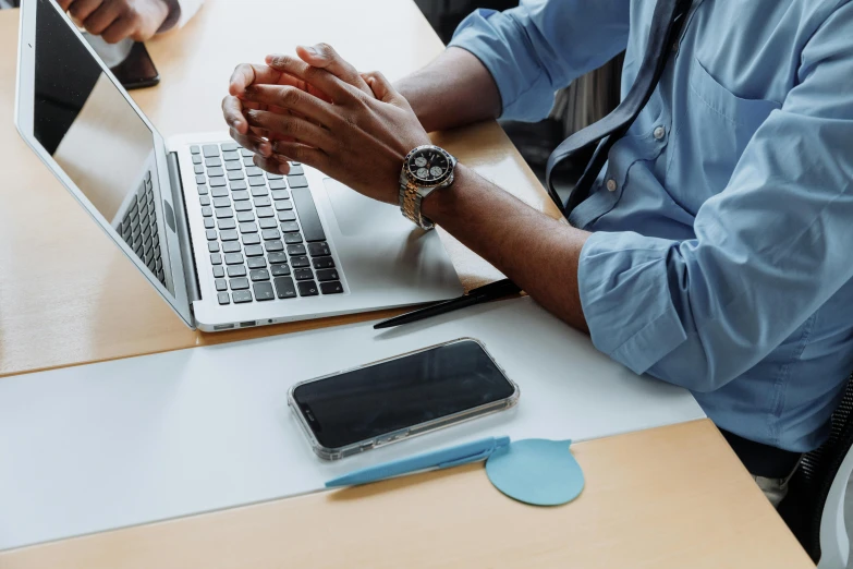 a person sitting at a desk with their laptop and holding hands with another person working on the computer