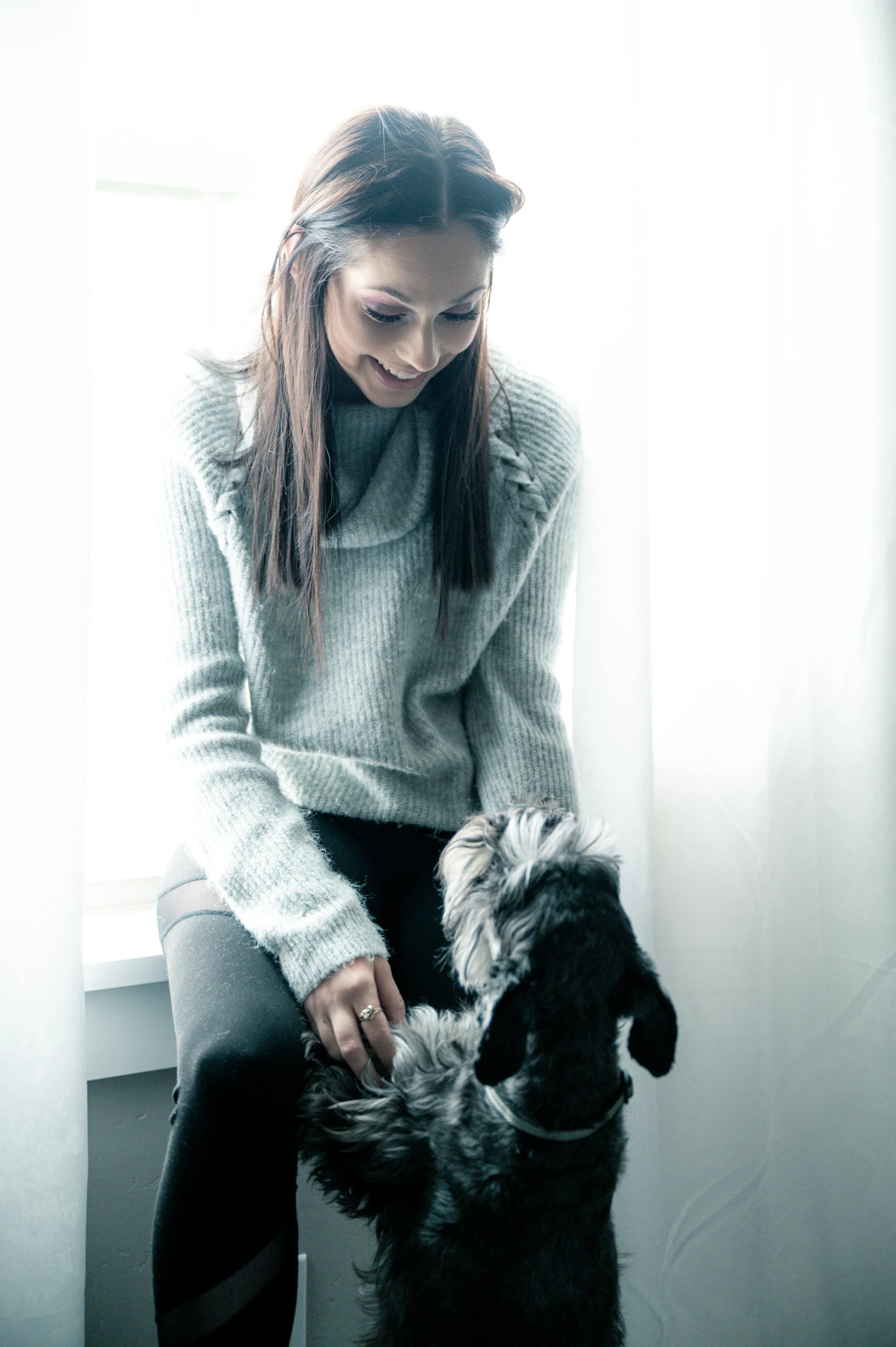 the woman sits on a window sill petting her dog