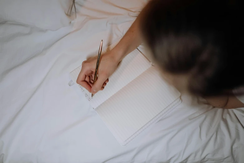 a woman is writing on her notebook while lying in bed