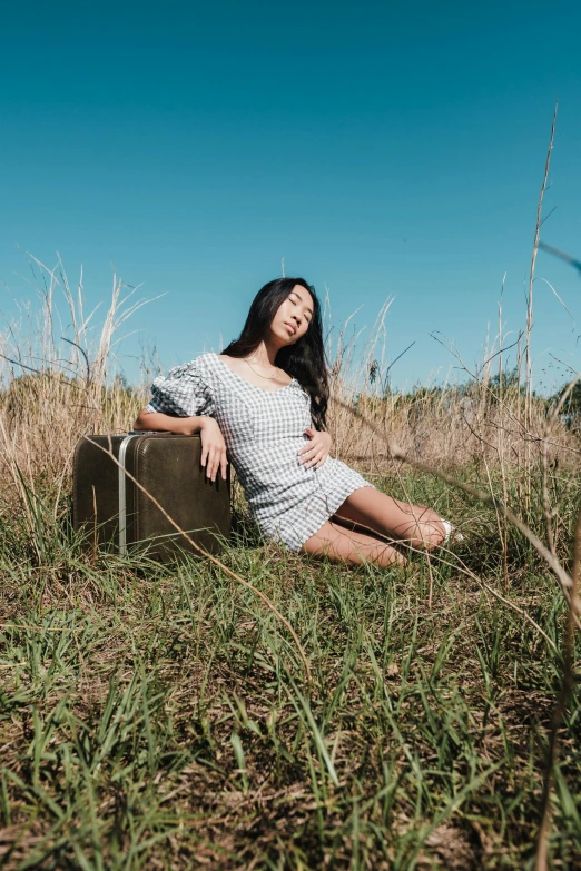 woman sitting on suitcase in tall grass on a sunny day