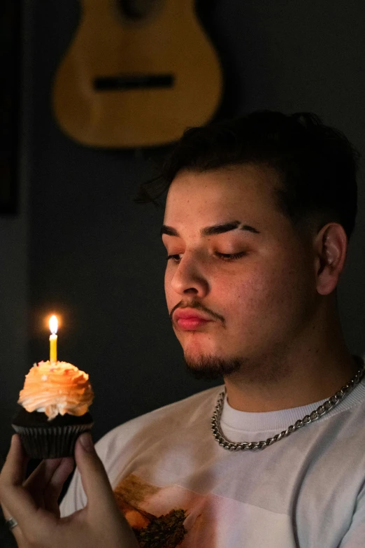 man eating cupcake and looking at a candle in his hand
