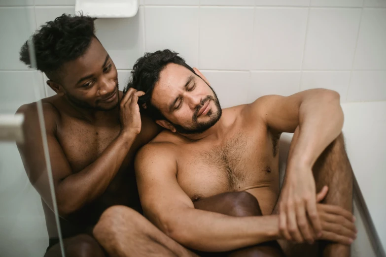 two shirtless men in the bathroom talking on the telephone