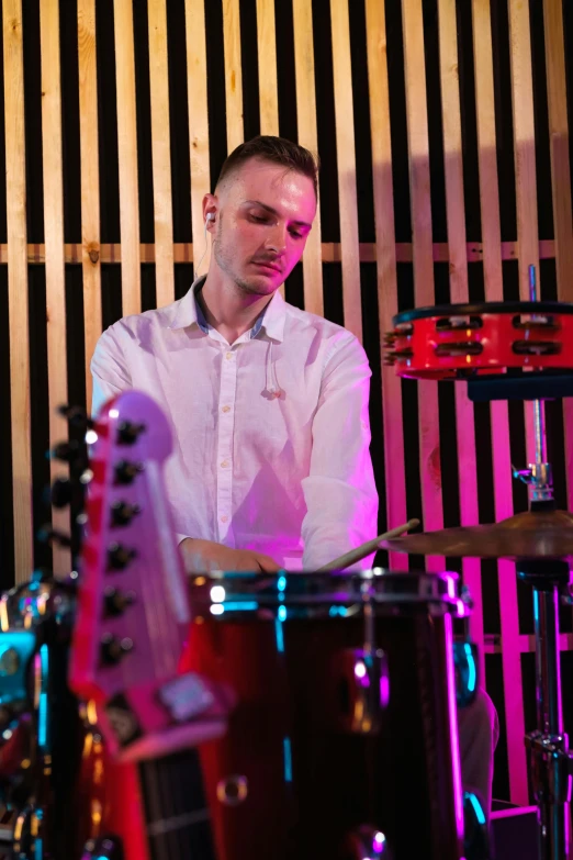 the young man in front of a drum set has a purple light on his face
