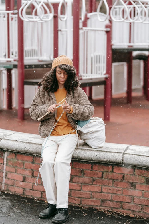 the woman is sitting on a brick wall and knitting