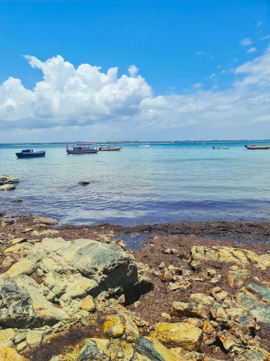 several boats on the water near rocks and blue sky