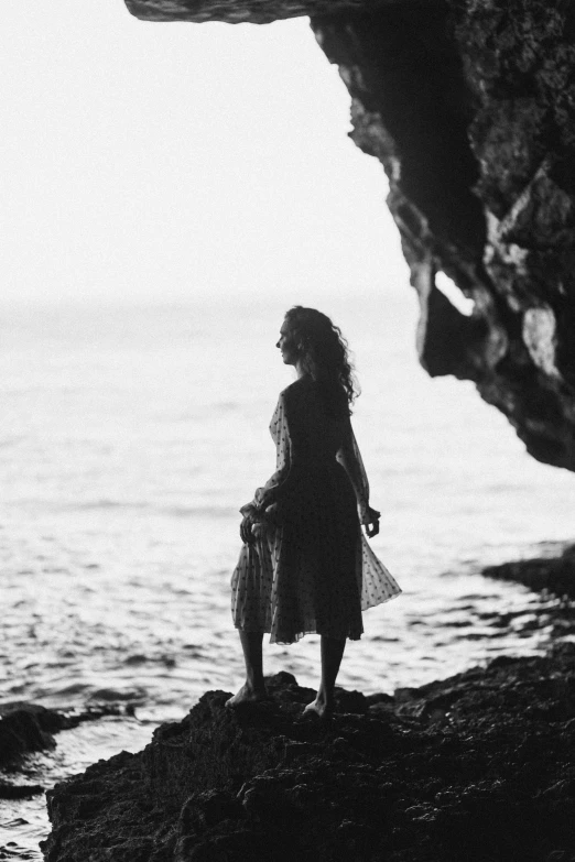 a woman standing on the rocks looking out over the water