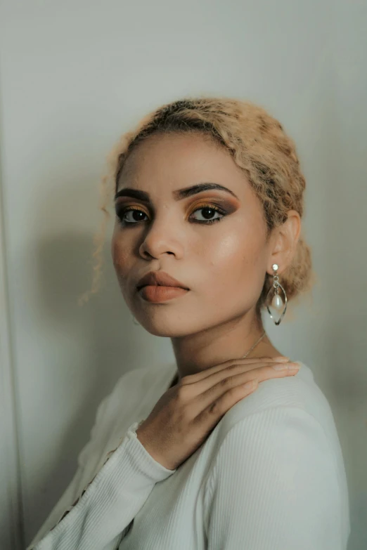 a beautiful young lady wearing statement earrings, standing against a wall