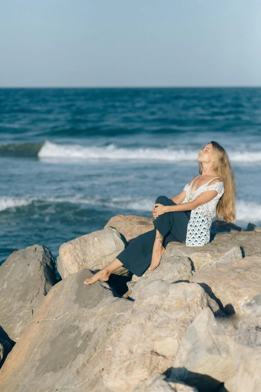 a woman sitting on top of rocks by the ocean