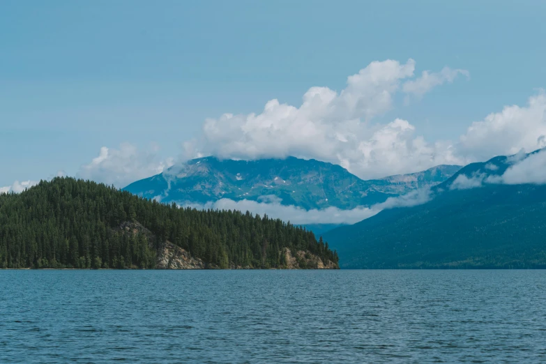 a mountain rises above water next to pine forest