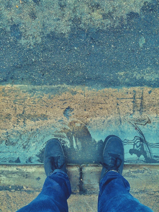 the top view of someone standing on a sidewalk with blue pants and shoes